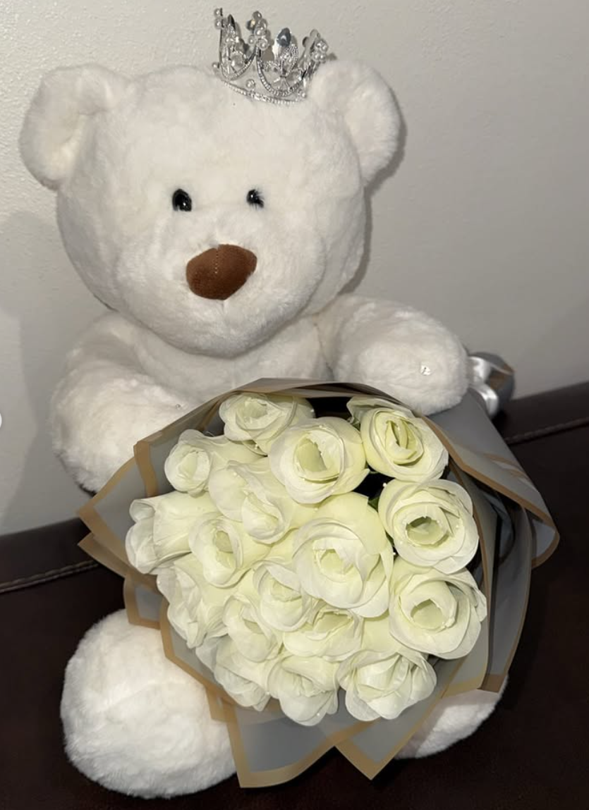 White teddy bear with crown holding a white rose bouquet